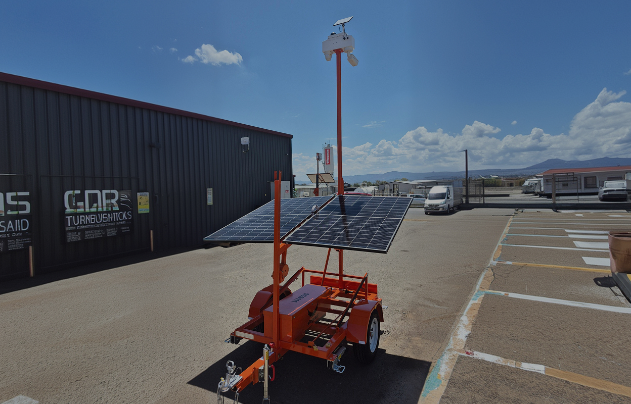 Orange mobile trailer equipped with solar panels and a camera mounted on a tall pole in an outdoor parking area.